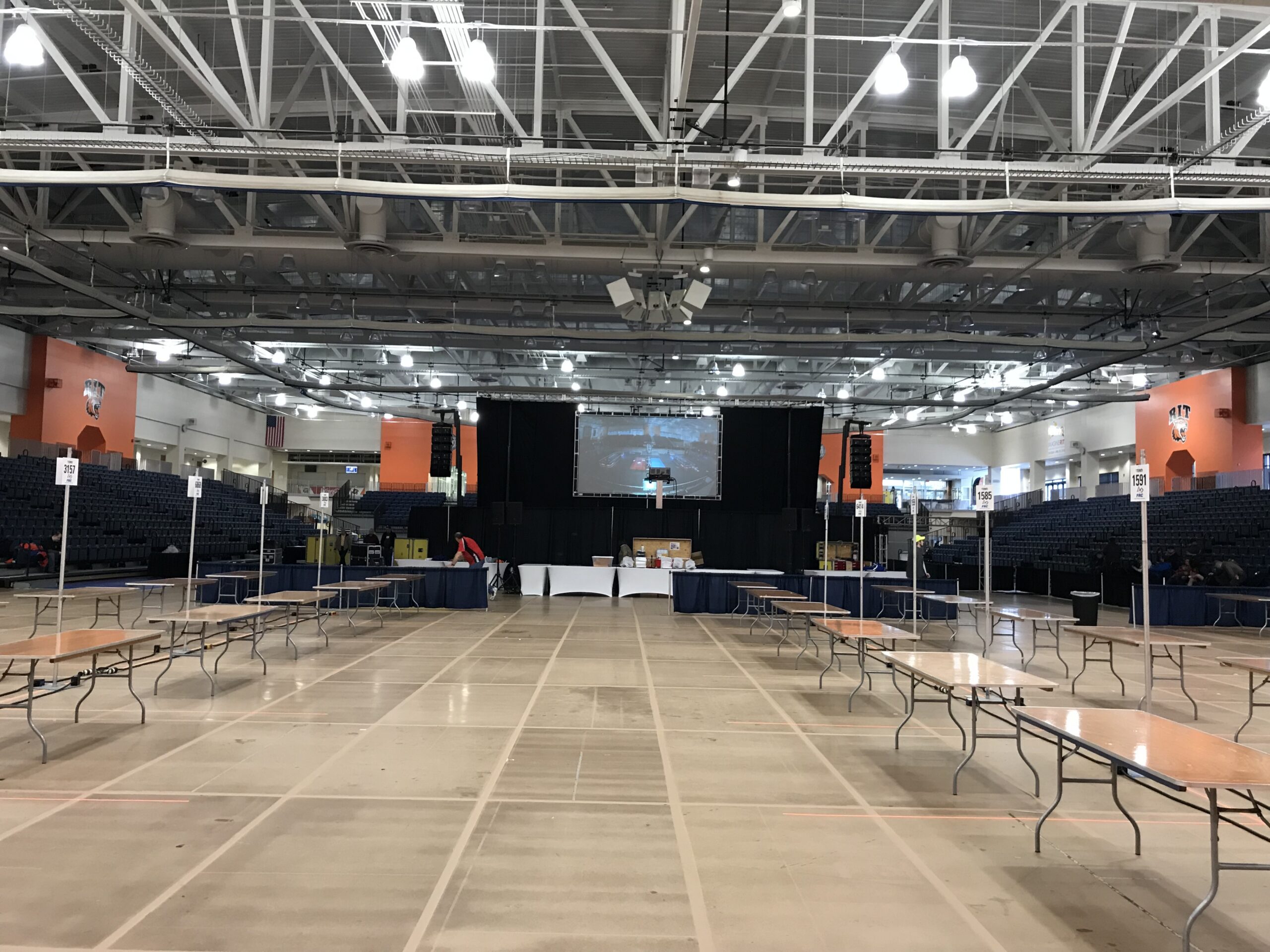 FIRST Robotics Competition Finger Lakes Regional at RIT during load-in, showing the arena floor, projection screen, drape, audio arrays and pit layout.