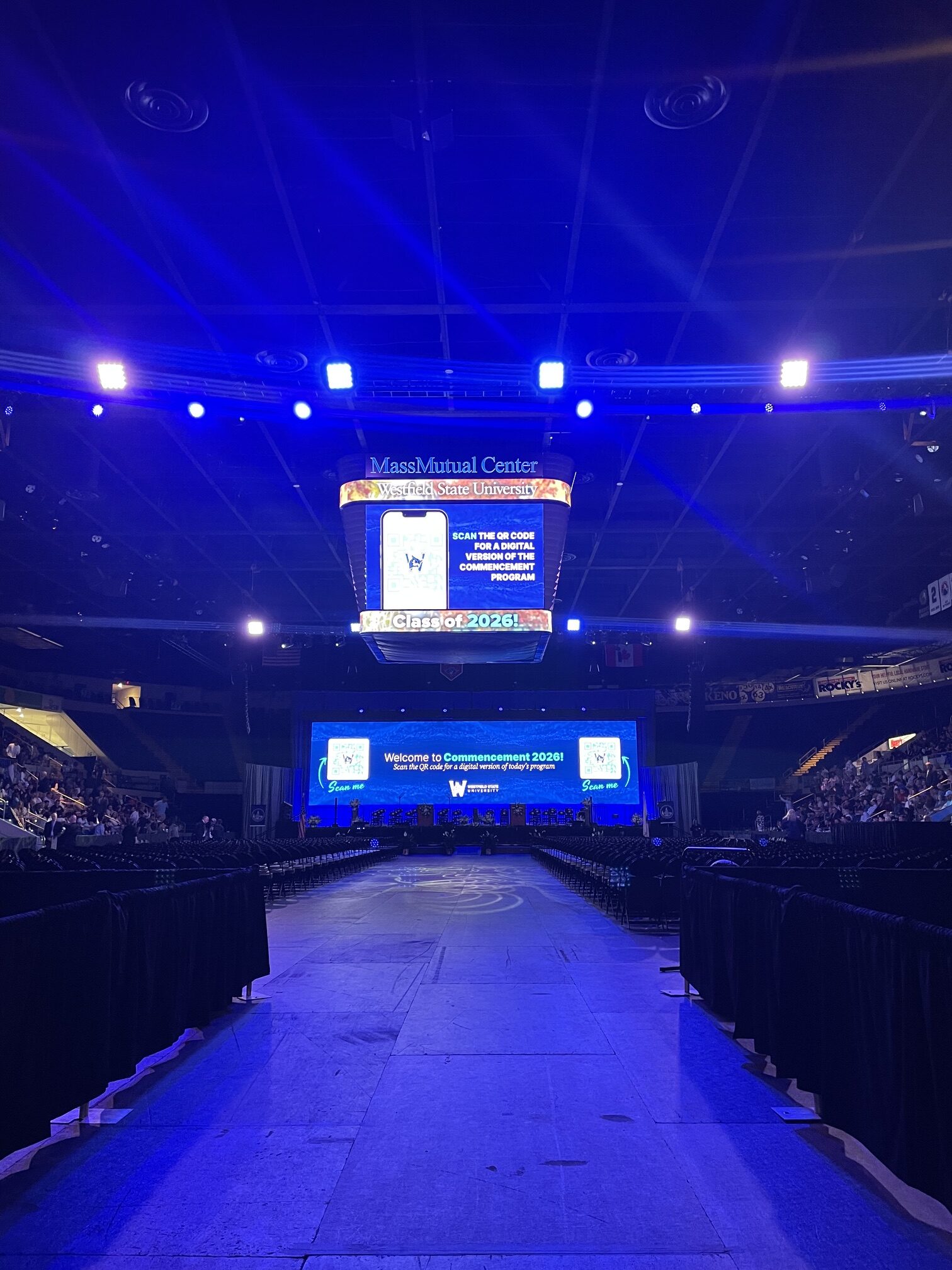 Large indoor commencement audience with stage video screens and event production